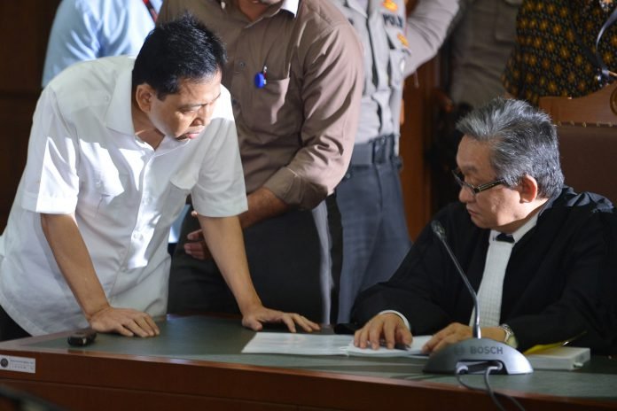 Terdakwa kasus dugaan korupsi KTP elektronik Setya Novanto (kiri) berbicara dengan penasehat hukumnya pada sidang perdana di gedung Pengadilan Tipikor Jakarta, Rabu (13/12).