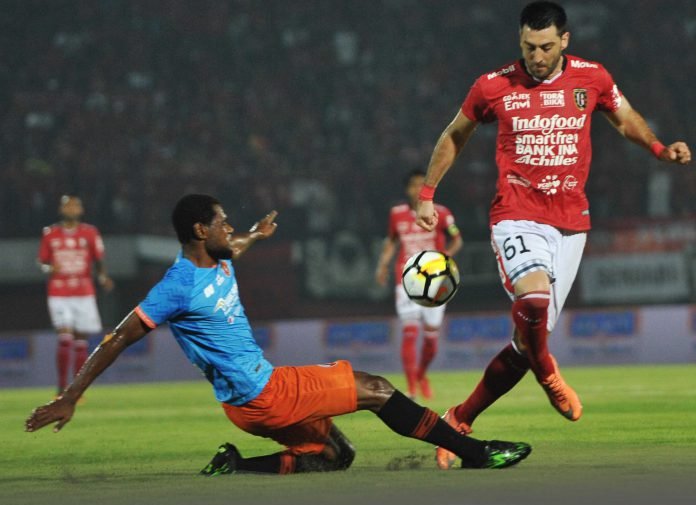 Pesepakbola Bali United Milos Krkotic (kanan) berebut bola dengan pesepak bola Perseru Serui Donny Harold Monim dalam pertandingan Sepak Bola Liga 1 2018 di Stadion I Wayan Dipta, Sabtu (7/4).